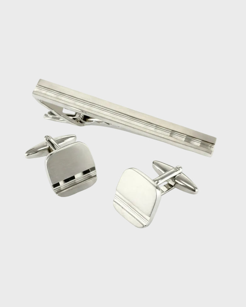 Silver cufflinks and tie clip set on a white background