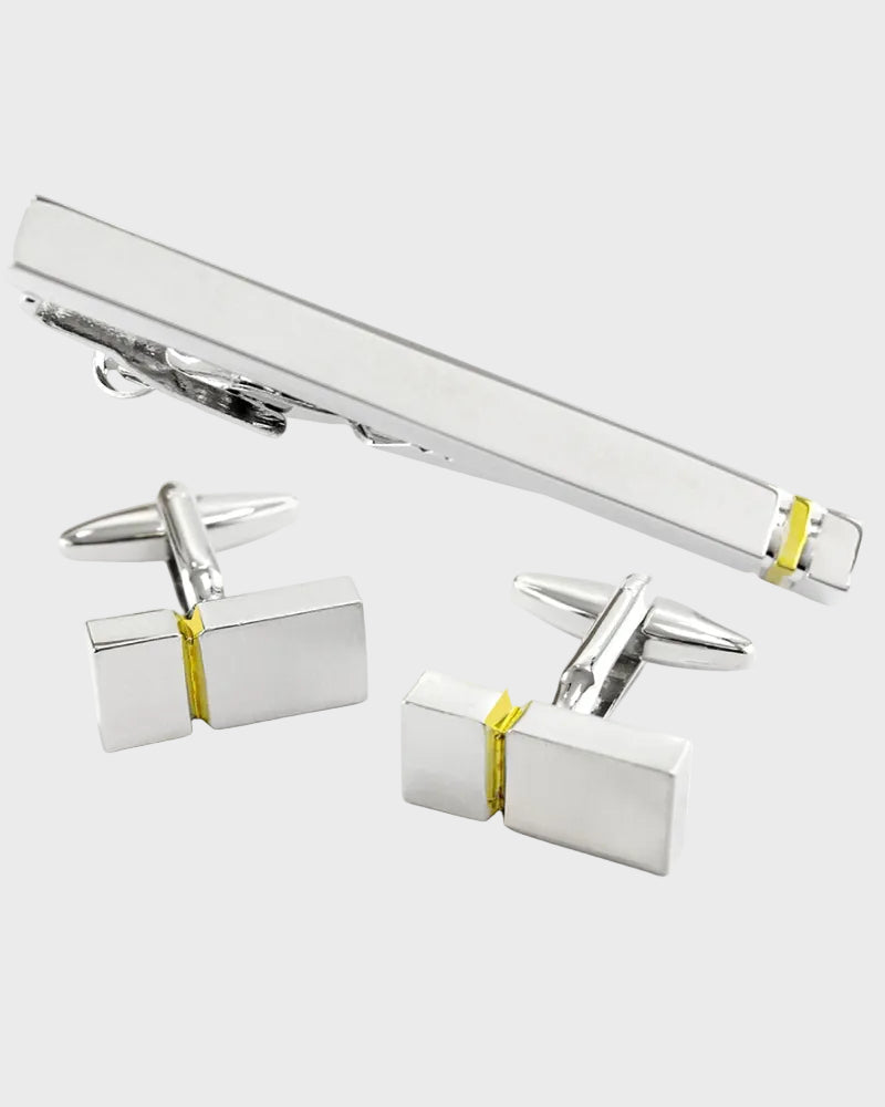 Silver cufflinks and tie clip set with gold accents on a white background