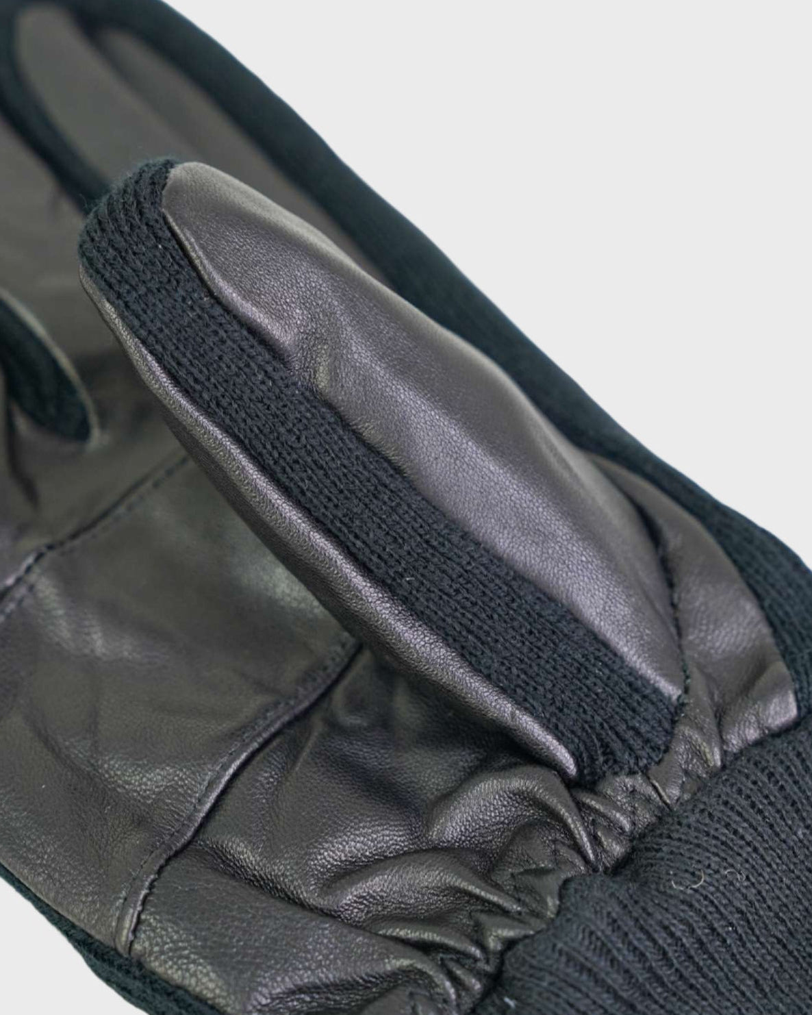 Close-up of black leather gloves with knitted cuffs on a light gray background