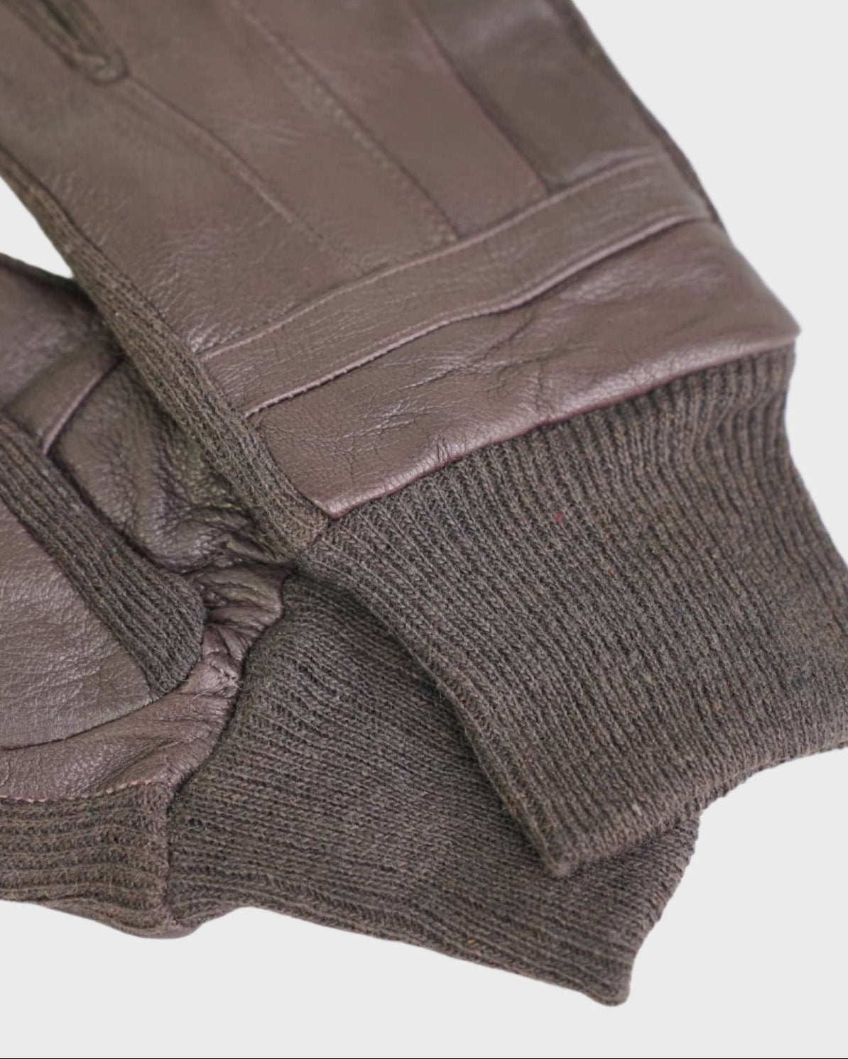 Brown leather gloves with knitted cuffs on a light gray background
