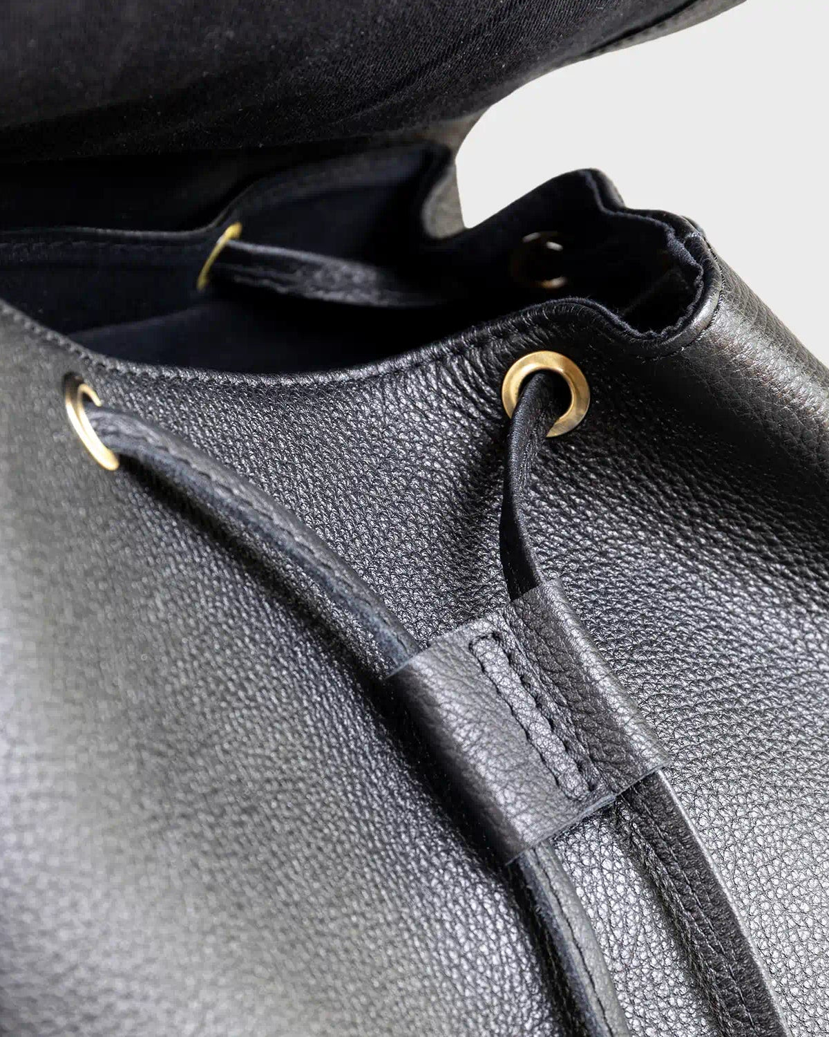 Close-up of a black leather bag with drawstring and visible brand logo.