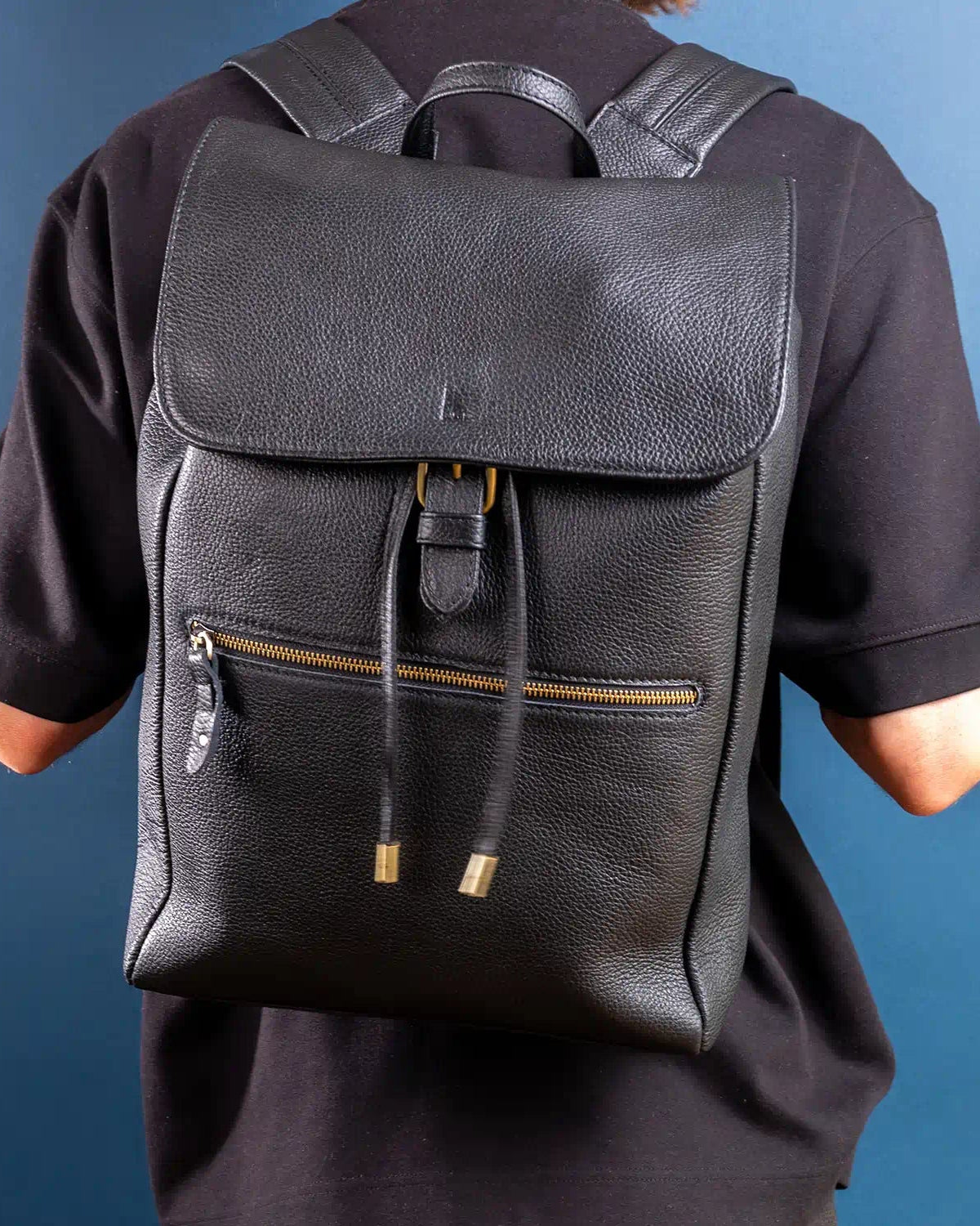 Person wearing a black leather backpack against a blue background