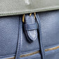 Close-up of a navy leather bag with gold zippers and a buckle.