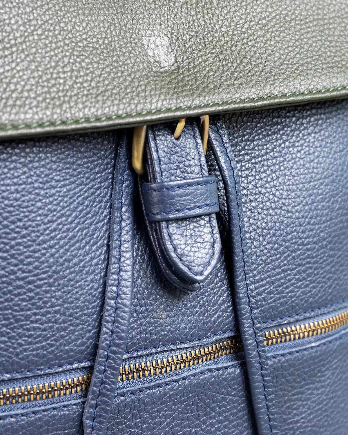 Close-up of a navy leather bag with gold zippers and a buckle.