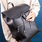 Person holding a black leather backpack against a blue background