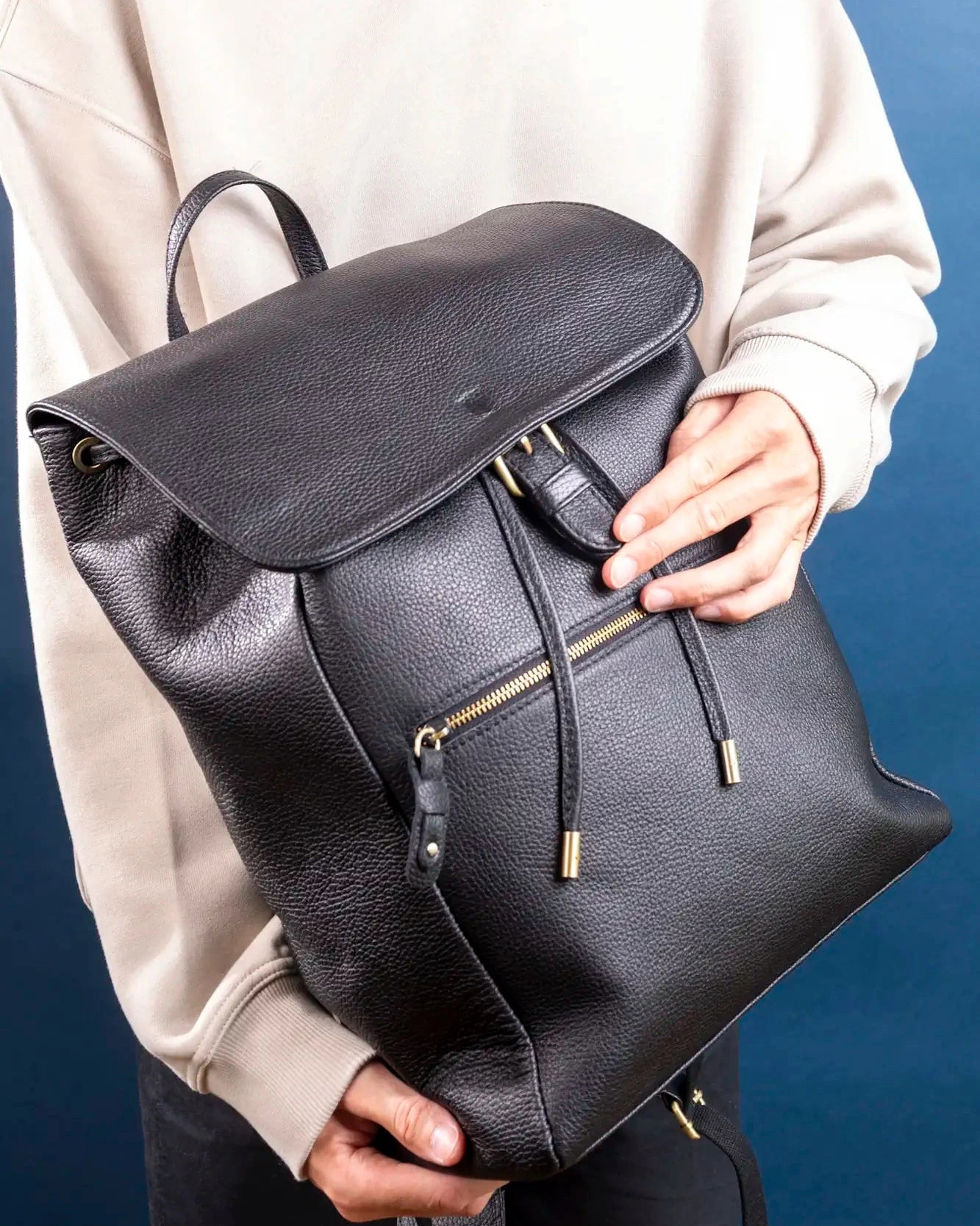 Person holding a black leather backpack against a blue background