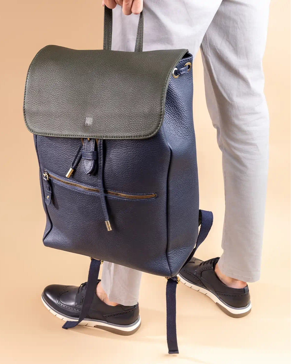 Person holding a navy blue backpack with a beige background