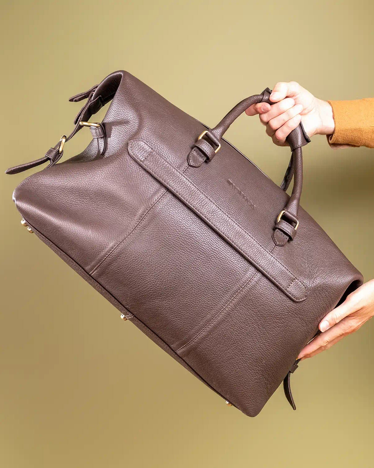 Brown leather holdall held by a person against a beige background