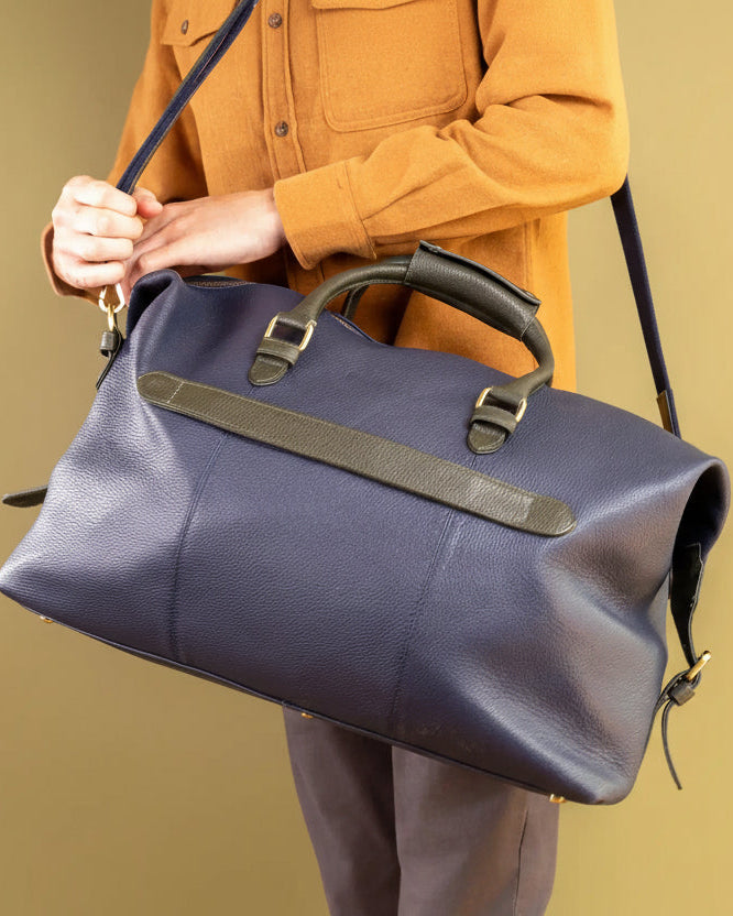 Person holding a navy holdall against a beige background
