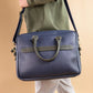 Blue leather briefcase with green handle held by a person against a beige background