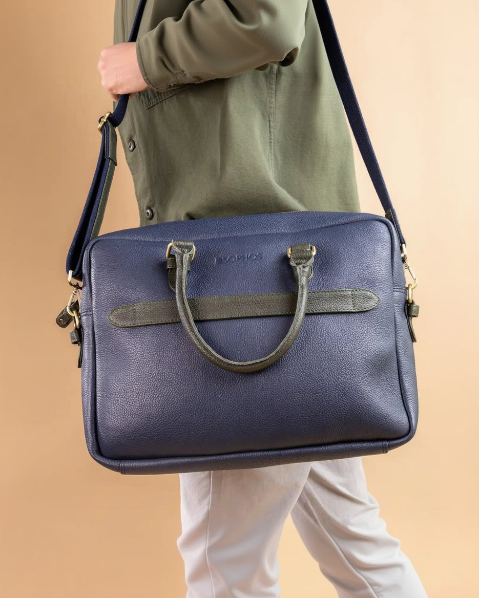 Blue leather briefcase with green handle held by a person against a beige background