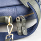 Close-up of a blue leather bag with green strap and gold hardware on a white background