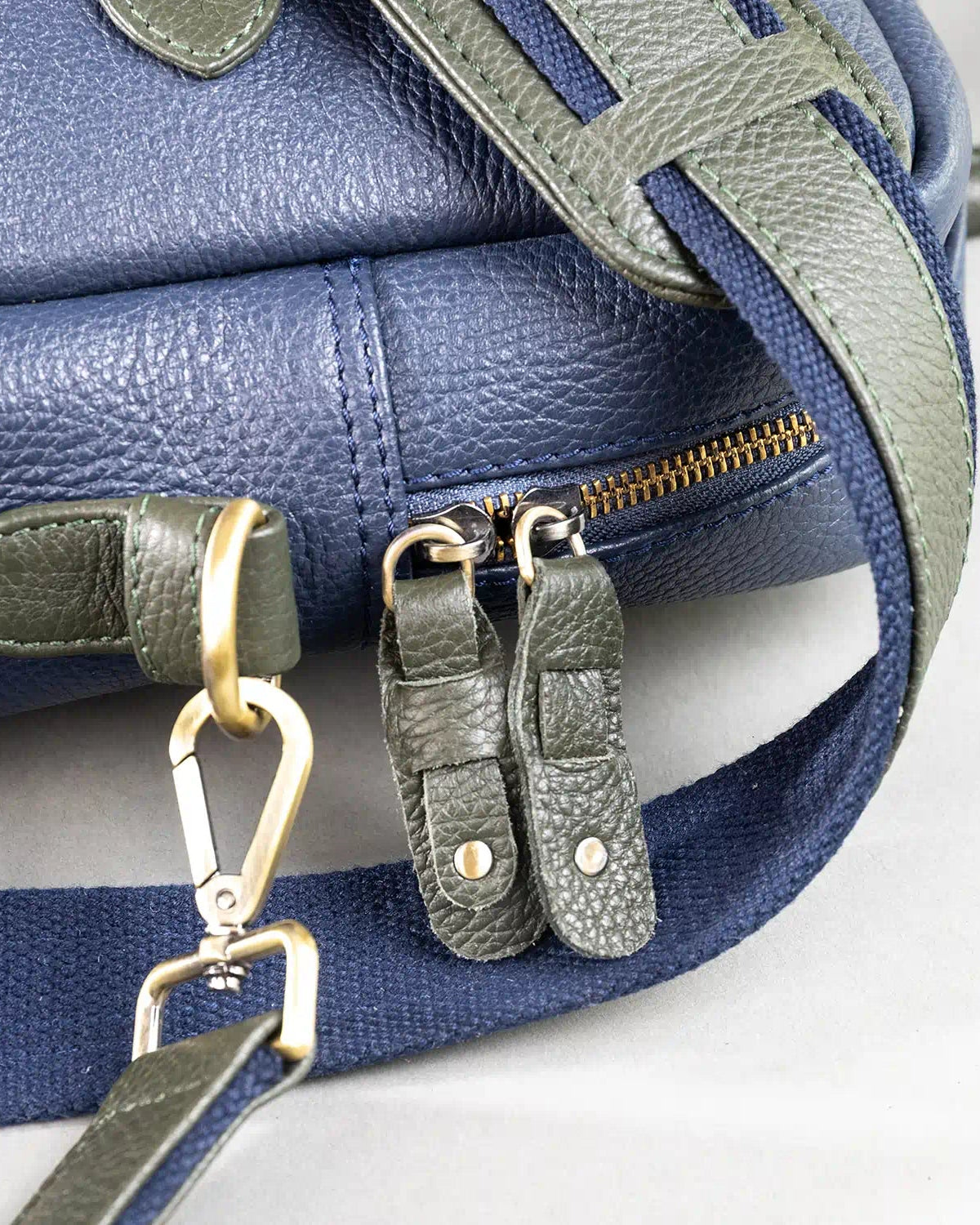 Close-up of a blue leather bag with green strap and gold hardware on a white background