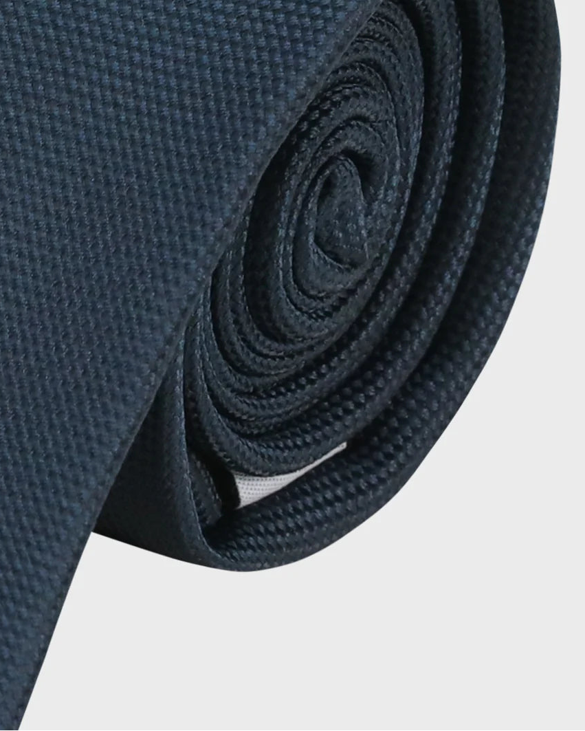 Navy blue tie rolled up on a light gray background
