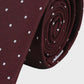 Maroon tie with white polka dots rolled up on a light gray background