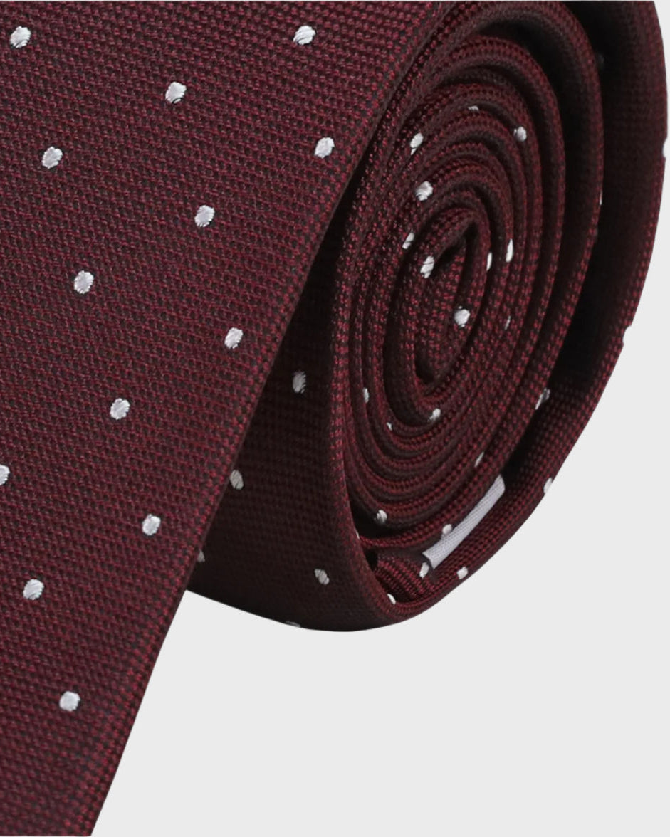 Maroon tie with white polka dots rolled up on a light gray background