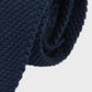 Rolled-up navy blue knitted tie on a light gray background