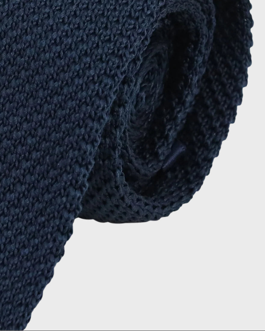 Rolled-up navy blue knitted tie on a light gray background