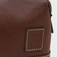 Close-up of a brown leather bag with a brand label on a light gray background