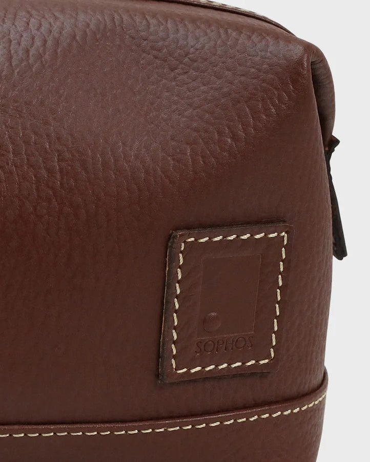 Close-up of a brown leather bag with a brand label on a light gray background