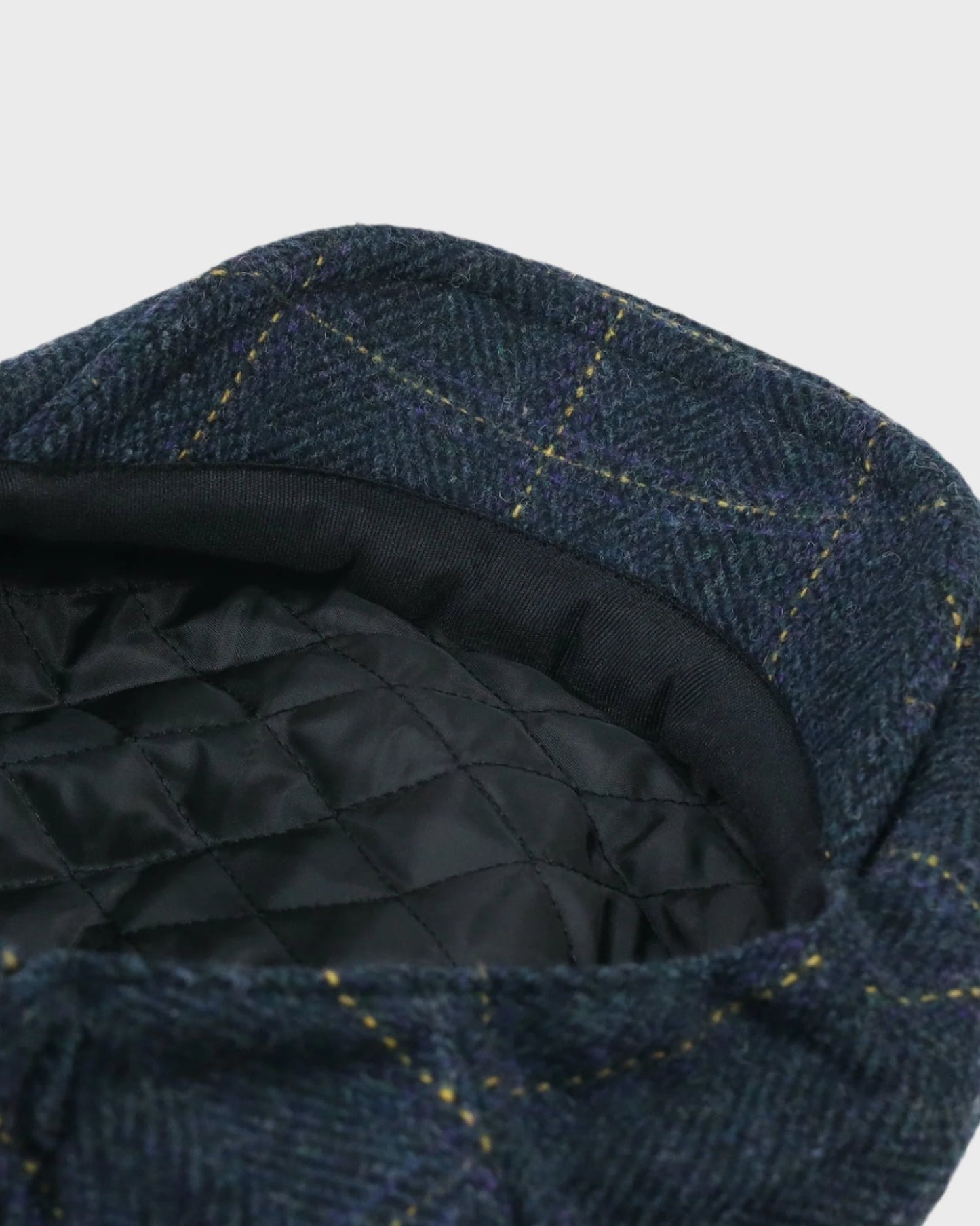 Blue checkered flat cap with black quilted interior on a light gray background