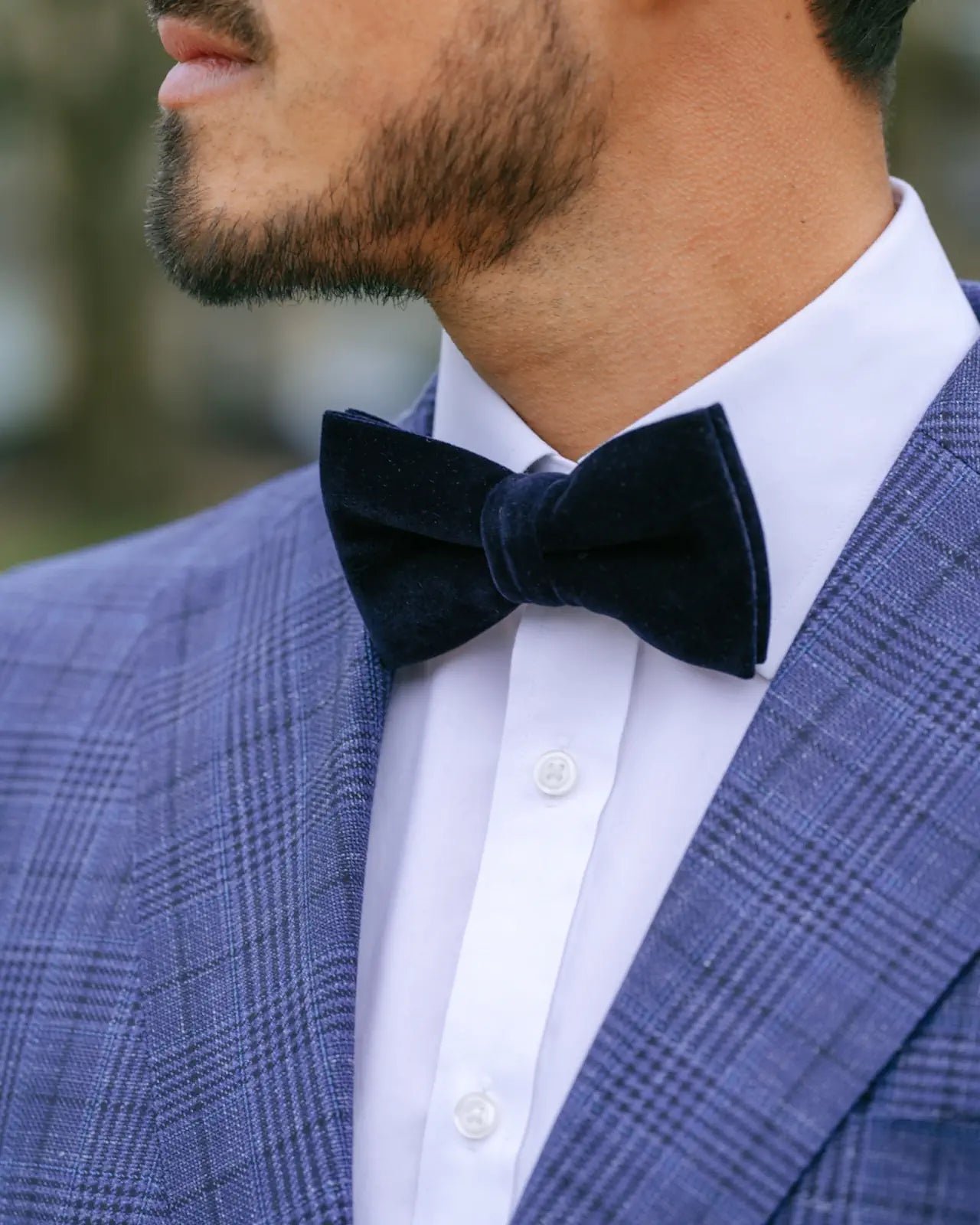 Man wearing a blue checkered suit with a white shirt and navy bow tie.